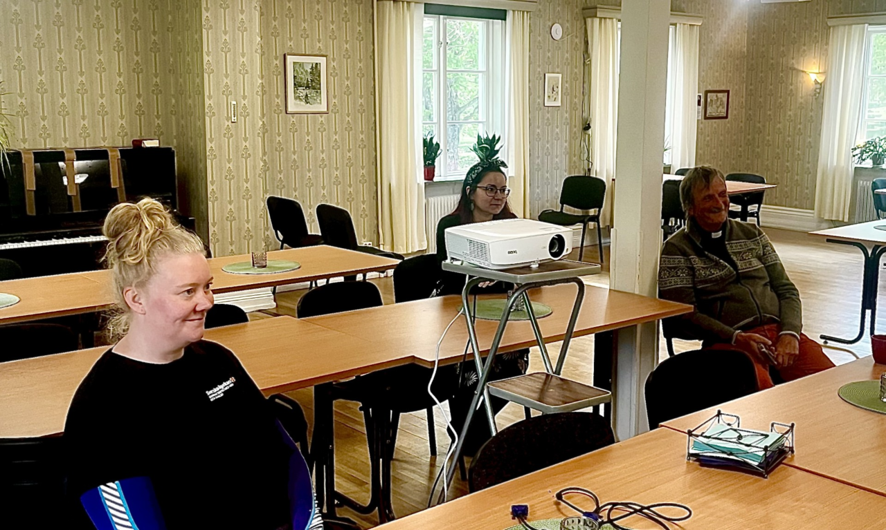 Tre personer från svenska kyrkan sitter vid bord och lyssnar på information om PDV.