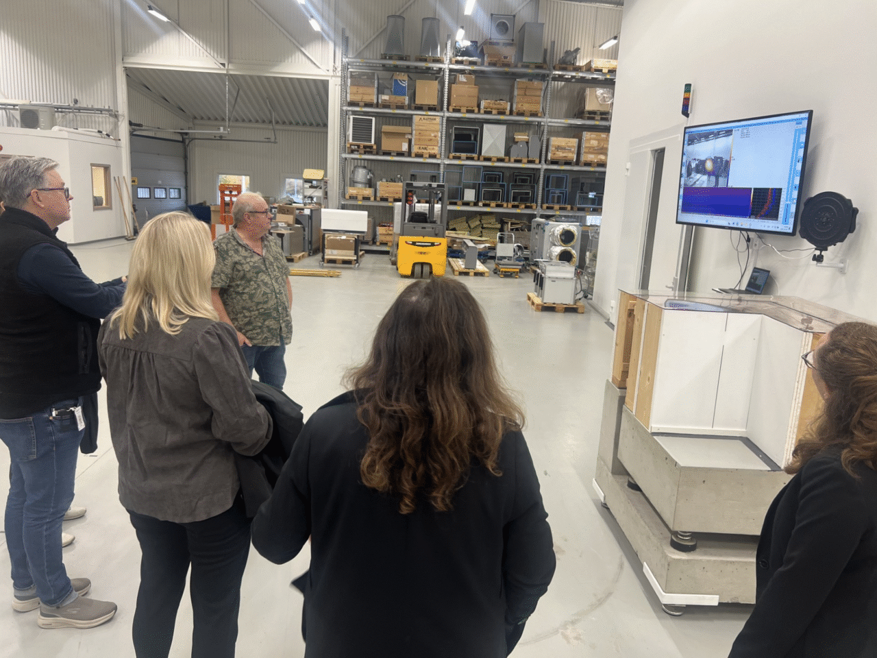 Rundvandring på en av Systemair anläggningar (TC - technical center). En man står och pratar och fyra andra personer står och lyssnar. Det är en steril och grå miljö.